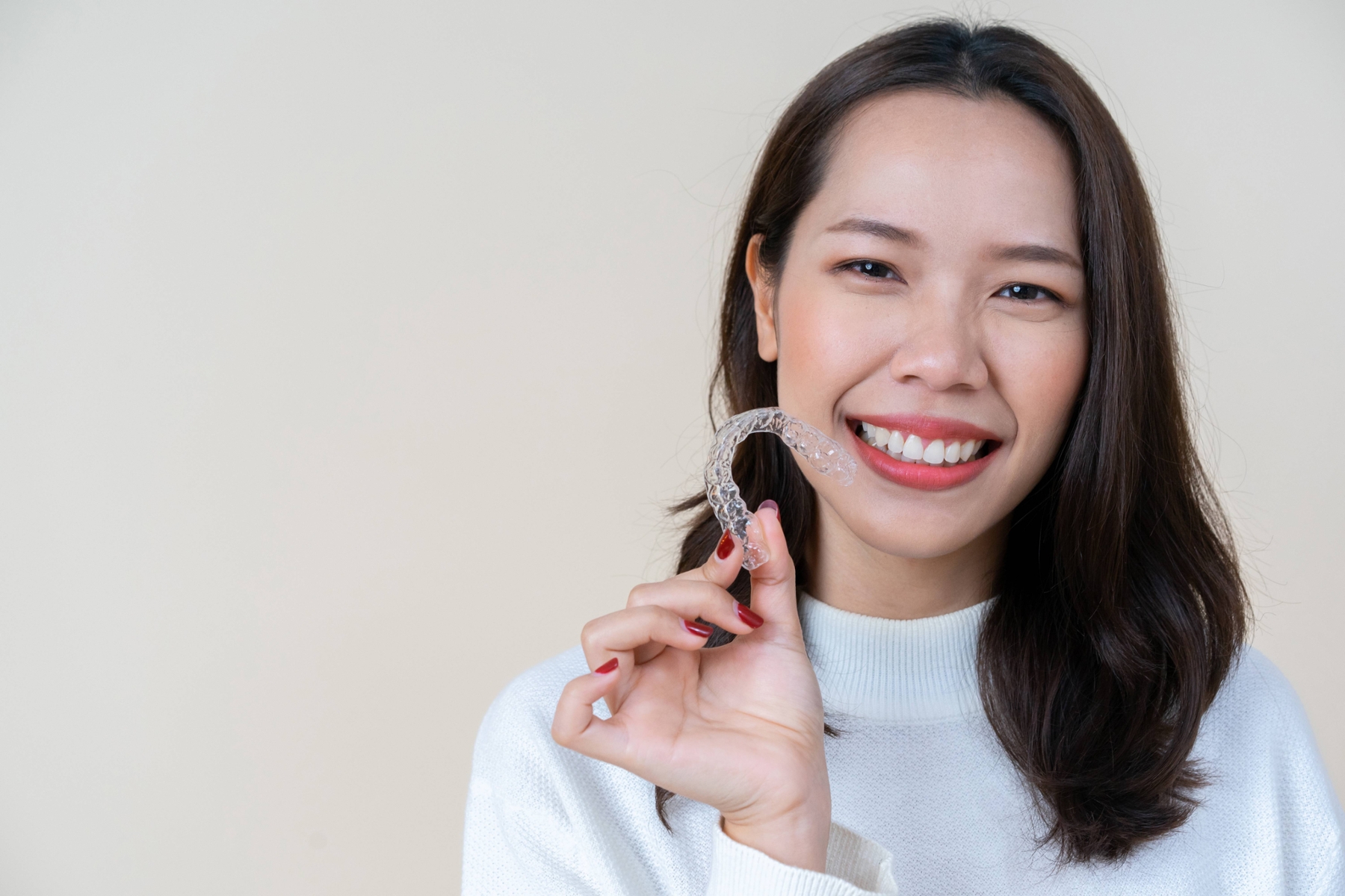 Smiling woman holding up an OrthoFX clear aligner tray at Golden Hill Family Dentistry in Lakewood, CO