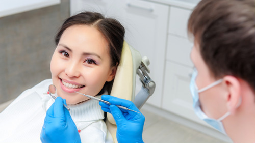 Smiling woman in dental chair during a preventive dental checkup with dentist holding tools