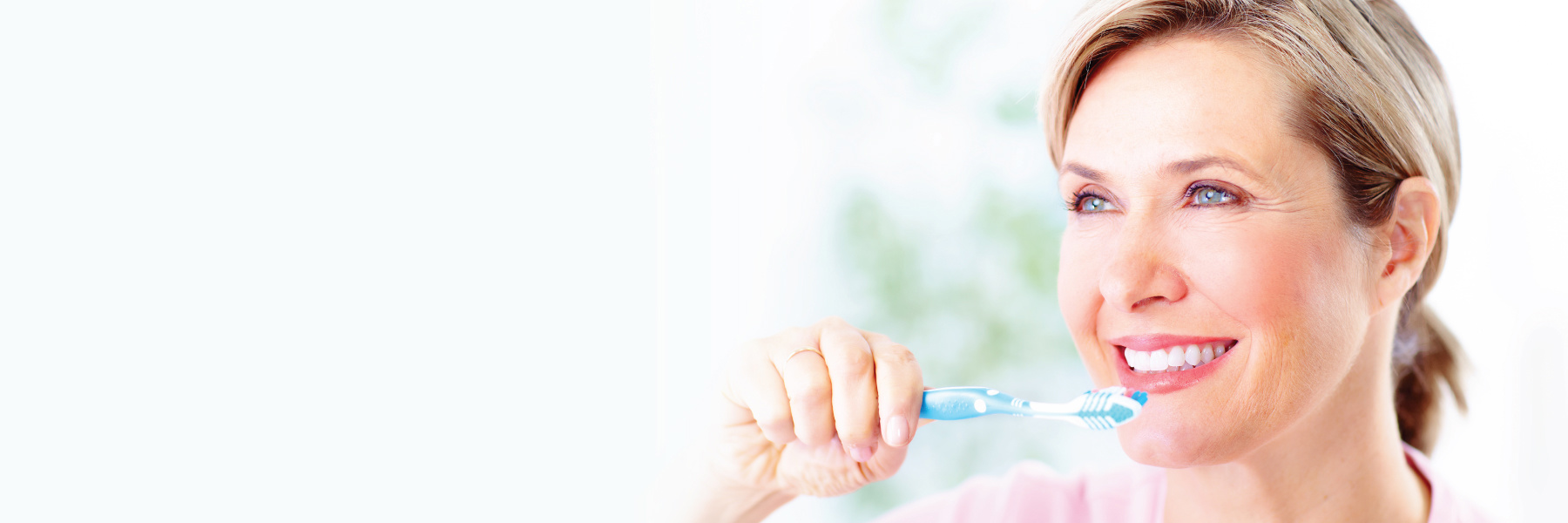 Smiling woman brushing teeth with blue toothbrush, practicing preventive dental care at home